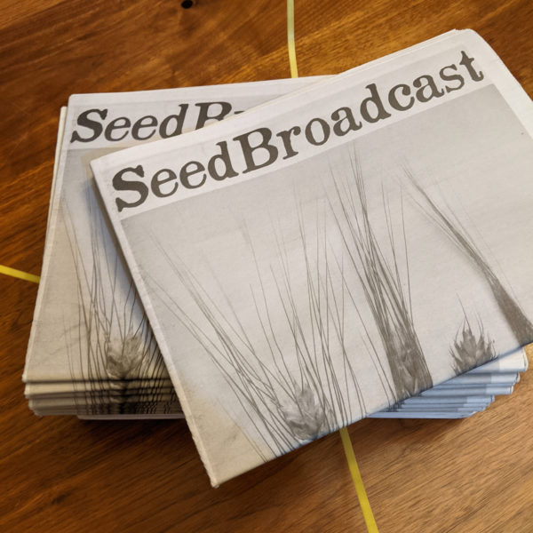 Staks of SeedBroadcast newsprint journals on wood tabletop
