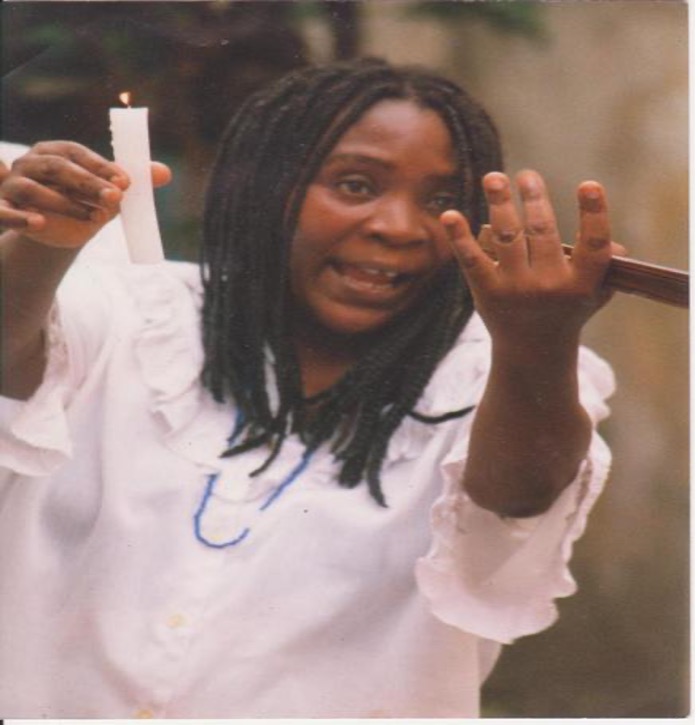 Afro-Cuban woman in a white dress holds a lit white candle and reaches toward the viewer.
