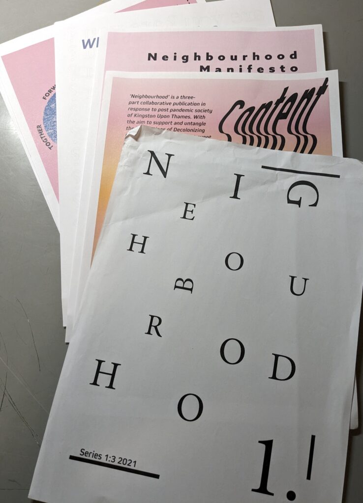 Loose papers making up the publications called "Neighbourhood 1. (Series 1:3 2021) by Merrydith Russell are spread out on a grey table.