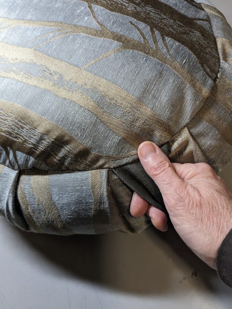 A hand is gripping a fabric handle attached to the side of a round, fabric meditation cushion.