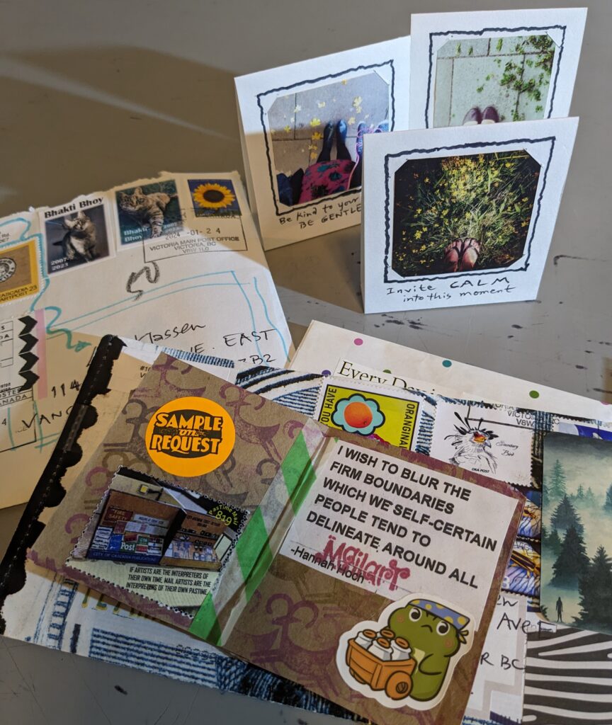 Mail art from Ginger Mason is spread out on a table. It includes three standing picture cards, the collage book and decorated envelopes.