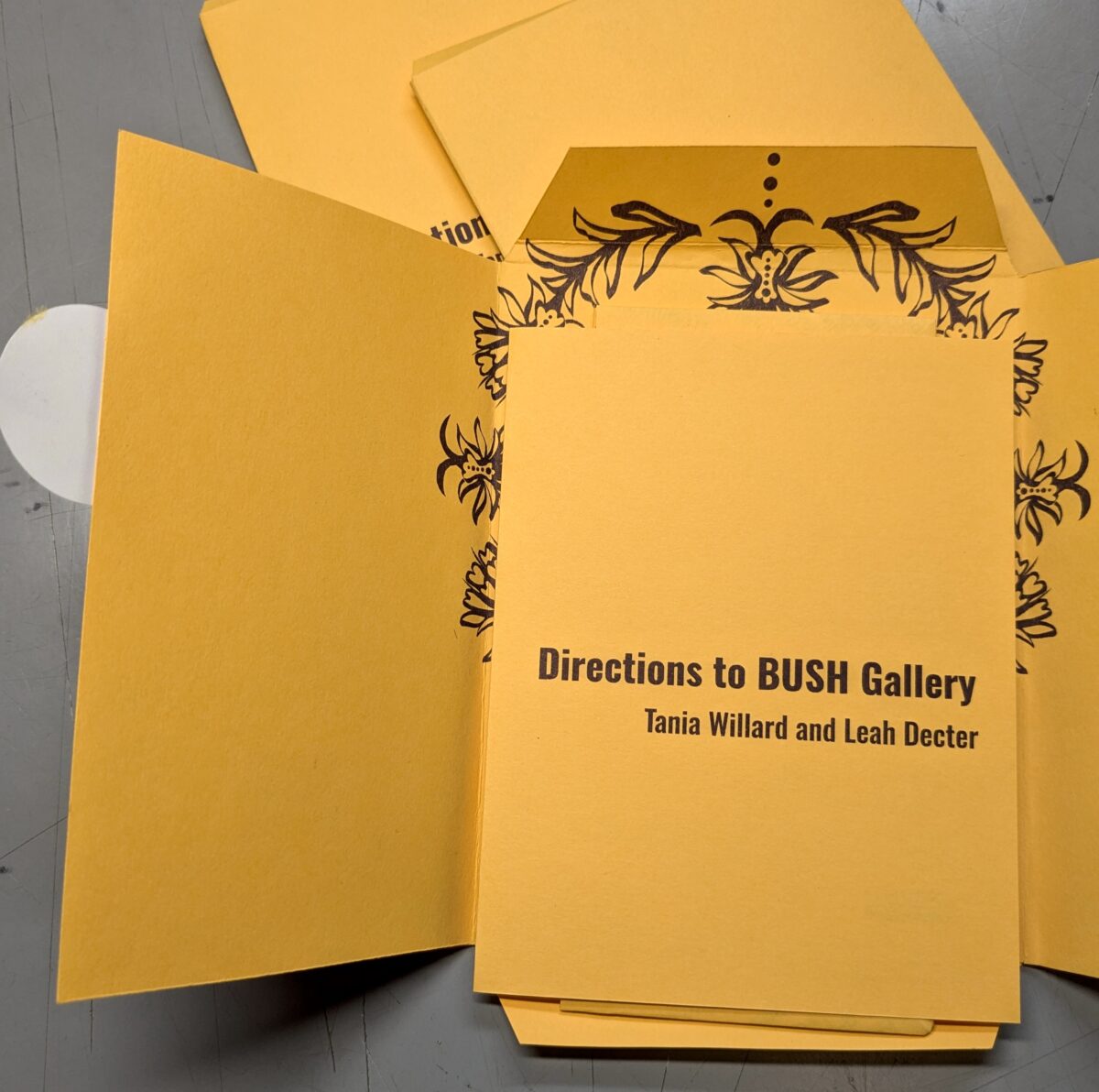 Photo of three components of the publication "Directions to BUSH Gallery" open and lying on a table.