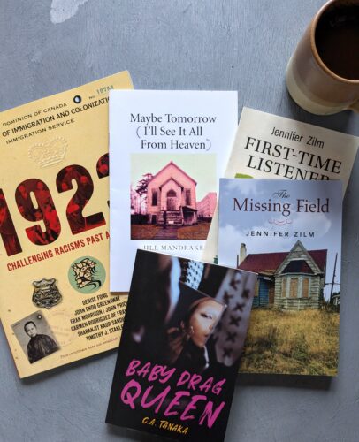 Five books are spread on a table with a pottery mug in the top right corner.