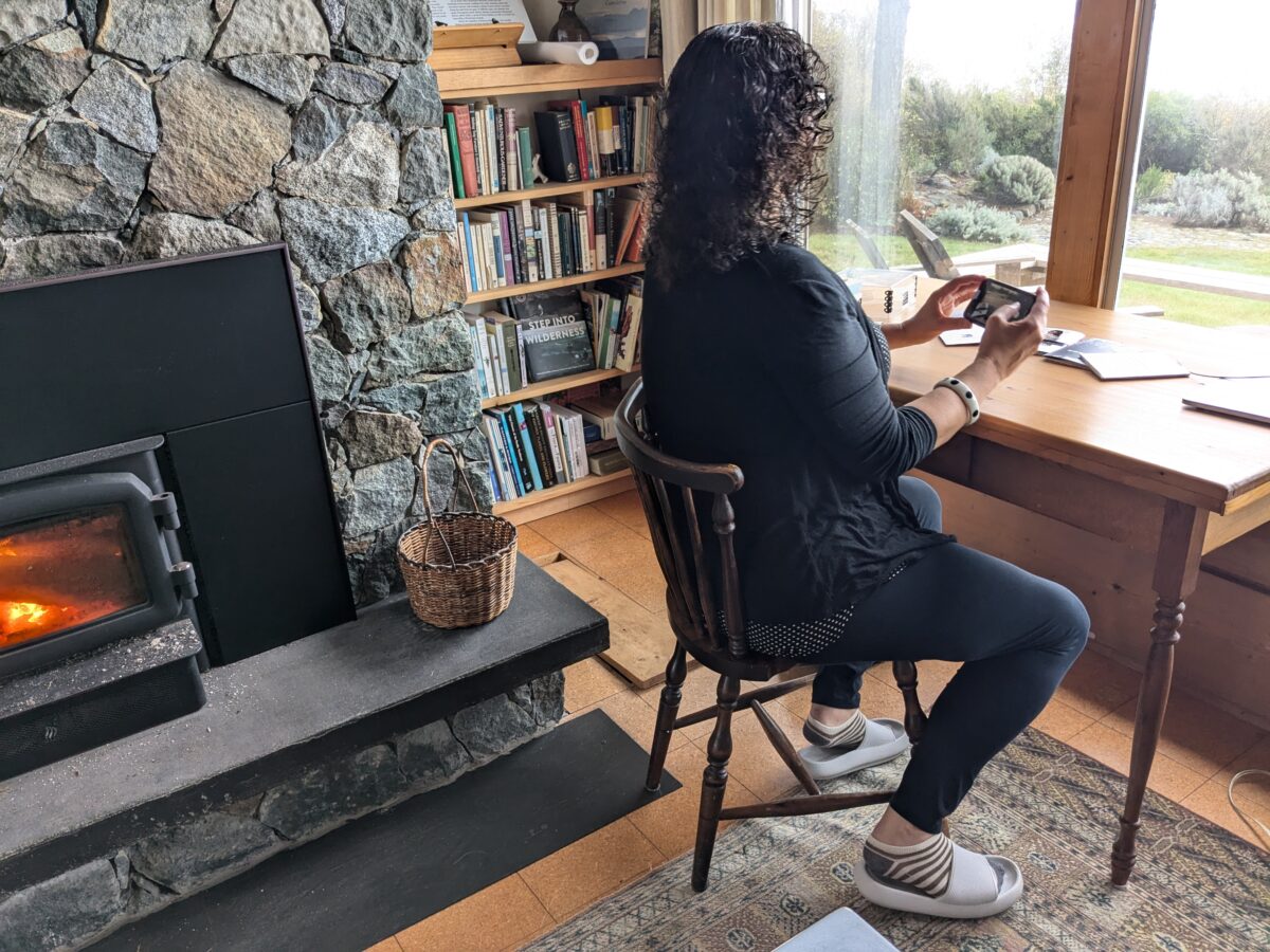 Deanne is sitting and photographing RML books, near a stone fireplace by a window overlooking the sea.