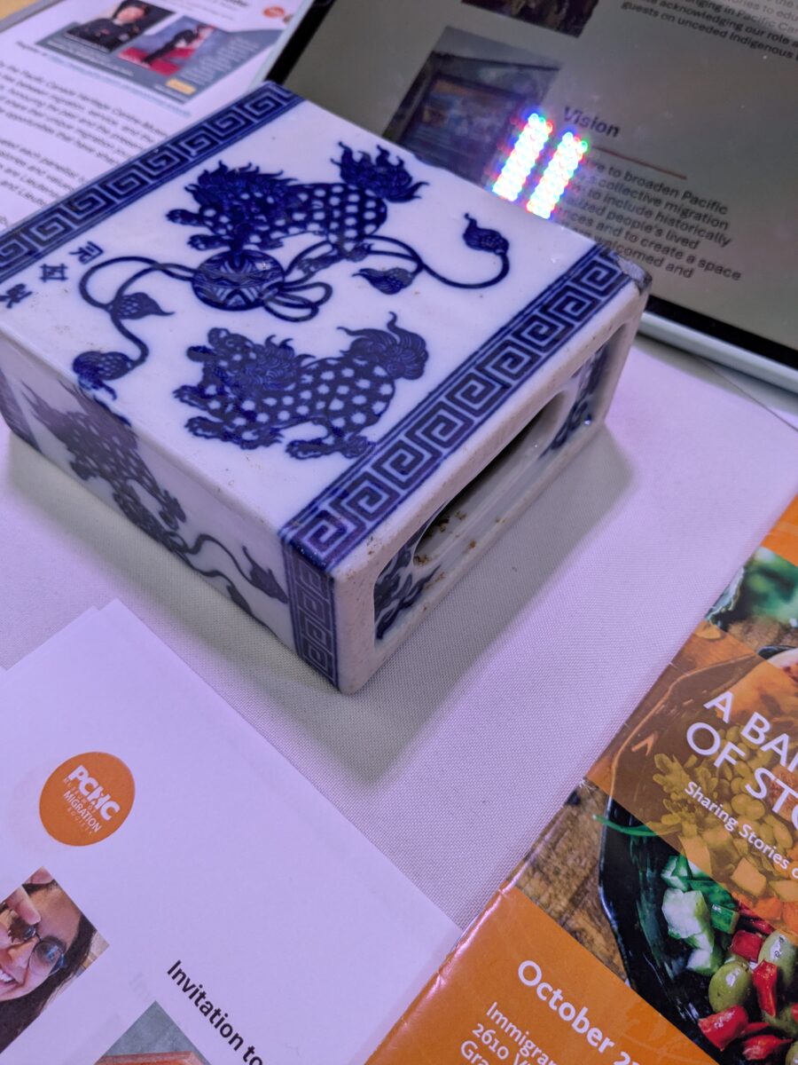 A small rectangular blue and white porcelain head rest or pillow sits on a table surrounded by pamphlets.